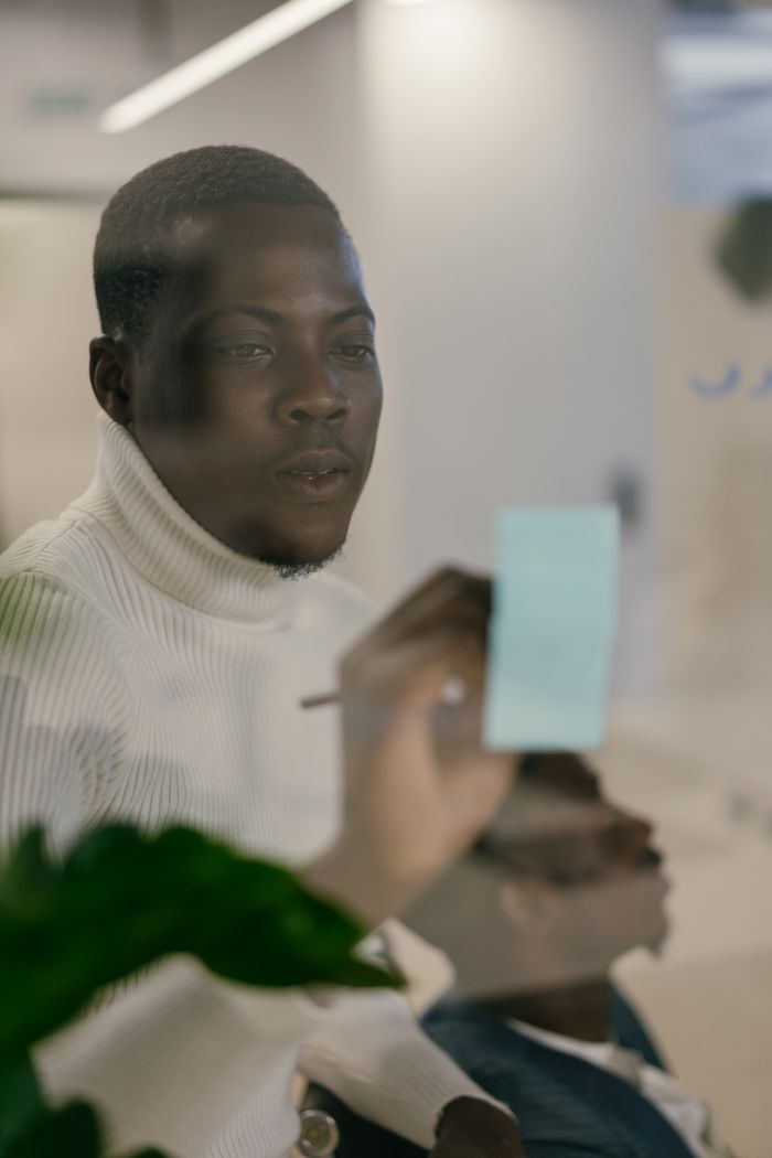 services-03 African American man writing notes on a glass board in an office setting.